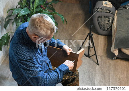 Man fixes wooden chair in a home setting with a plant nearby Man fixes wooden chair in a home setting with a plant nearby 137579601
