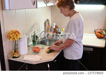 Woman prepares a sandwich in a kitchen with fresh vegetables and fruit on the counter 137579605
