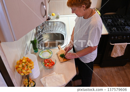 Person prepares vegetables in kitchen while standing near sink Person prepares vegetables in kitchen while standing near sink 137579606