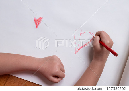 Child drawing hearts on white paper with red pencil Child drawing hearts on white paper with red pencil 137580202