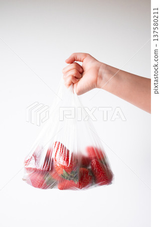 Hand holding bag of fresh strawberries against white background 137580211