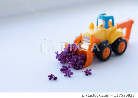 Toy backhoe with lilac flowers. Closeup, selective focus. Toy backhoe with lilac flowers. Closeup, selective focus. 137580922