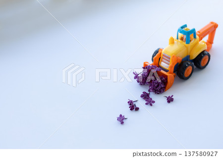 Toy backhoe with lilac flowers. Closeup, selective focus. Toy backhoe with lilac flowers. Closeup, selective focus. 137580927