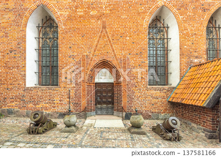 The Malbork Castle, a brick Gothic castle in northern Poland, Europe. Historic building facade featuring brickwork, arched windows, cannons, and stone accents creating an imposing historical ambiance. 137581166