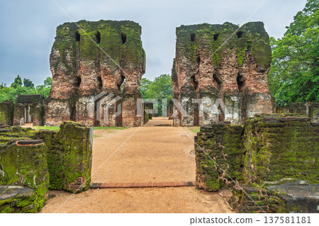 Ancient Royal Palace Ruins in Polonnaruwa, Sri Lanka. Ancient brick ruins with overgrown moss, leading to a path between two weathered historical structures under a cloudy sky Ancient Royal Palace Ruins in Polonnaruwa, Sri Lanka. Ancient brick ruins with overgrown moss, leading to a path between two weathered historical structures under a cloudy sky 137581181