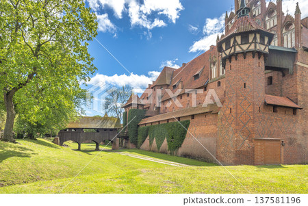 The Malbork Castle, a brick Gothic castle in northern Poland, Europe. Majestic castle featuring medieval architecture, brick walls, turrets, and a wooden bridge on a bright, sunny day. The Malbork Castle, a brick Gothic castle in northern Poland, Europe. Majestic castle featuring medieval architecture, brick walls, turrets, and a wooden bridge on a bright, sunny day. 137581196
