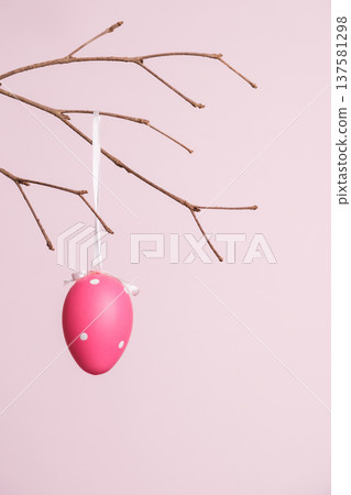 Pink Easter egg hanging from branch against a pastel pink background 137581298