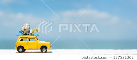 Yellow toy car with luggage on roof against blue sky and ocean backdrop Yellow toy car with luggage on roof against blue sky and ocean backdrop 137581302