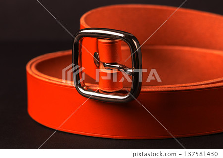 A belt with a silver buckle is orange in color. The belt is made of leather and has a square buckle A belt with a silver buckle is orange in color. The belt is made of leather and has a square buckle 137581430