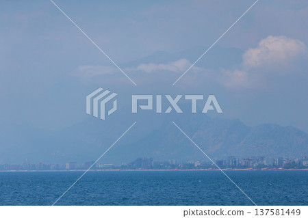 A landscape with a blue sea and a city blurred in the distance near a mountain. A landscape with a blue sea and a city blurred in the distance near a mountain. 137581449