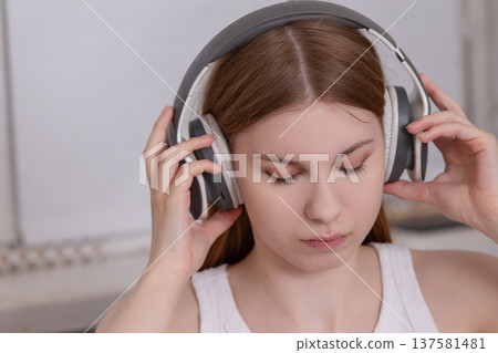 Young woman wearing headphones while listening to music in a cozy indoor environment during the afternoon 137581481