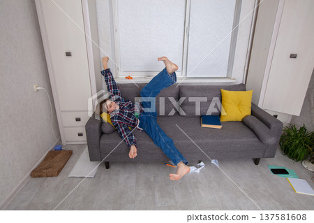 Child playfully falling off a couch in a cluttered living room 137581608