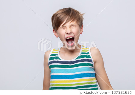Young boy expressing excitement while shouting in a striped tank top against a plain background Young boy expressing excitement while shouting in a striped tank top against a plain background 137581655