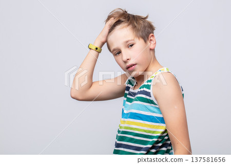 Young boy poses stylishly against a neutral background showcasing playful expression and casual fashion in bright stripes Young boy poses stylishly against a neutral background showcasing playful expression and casual fashion in bright stripes 137581656