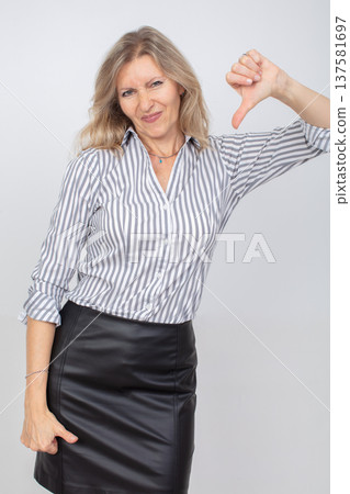 Woman expressing disapproval in a striped shirt and leather skirt against a plain background Woman expressing disapproval in a striped shirt and leather skirt against a plain background 137581697