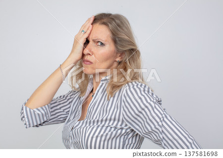 Frustrated woman in a striped shirt wearing a concerned expression against a light background Frustrated woman in a striped shirt wearing a concerned expression against a light background 137581698
