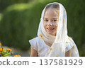 Young girl wearing a scarf smiles in a garden during daylight, surrounded by blooming flowers 137581929