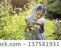 Young girl exploring flowers in a sunny garden during springtime while wearing a scarf and a joyful smile 137581931