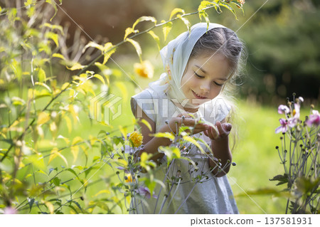 Young girl exploring flowers in a sunny garden during springtime while wearing a scarf and a joyful smile 137581931