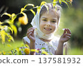 Young girl smiles while holding petals in a lush garden during a sunny afternoon 137581932