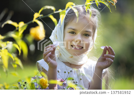 Young girl smiles while holding petals in a lush garden during a sunny afternoon 137581932