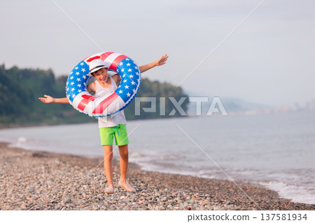 Child enjoying playing on beach with inflatable ring in american flag colors on sunny day 137581934