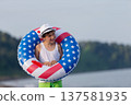 Child enjoying playing on beach with inflatable ring in american flag colors on sunny day 137581935