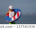 Child enjoying playing on beach with inflatable ring in american flag colors on sunny day 137581936
