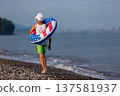 A boy walks along the beach with an inflatable ring in the colors of the American flag on a summer morning near the shore 137581937