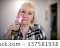 Woman holding a pink and white rose while looking thoughtfully in a cozy indoor setting 137581938