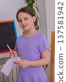 Young girl holding a pen and paper in a classroom, preparing to write during an art activity in the afternoon 137581942