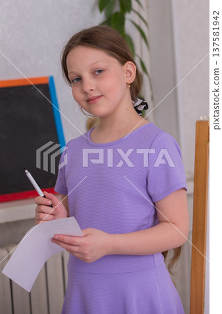 Young girl holding a pen and paper in a classroom, preparing to write during an art activity in the afternoon Young girl holding a pen and paper in a classroom, preparing to write during an art activity in the afternoon 137581942