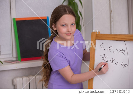 Young girl joyfully solving math problems on a chalkboard in a bright classroom setting Young girl joyfully solving math problems on a chalkboard in a bright classroom setting 137581943
