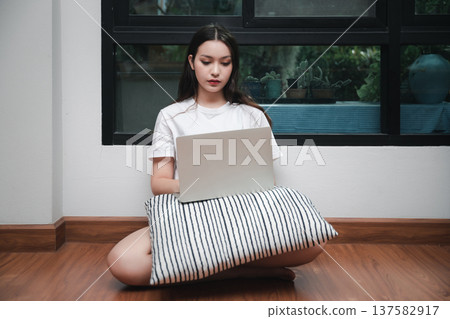 A young woman with laptop and pillow sitting drowsy on the living room floor. A young woman with laptop and pillow sitting drowsy on the living room floor. 137582917