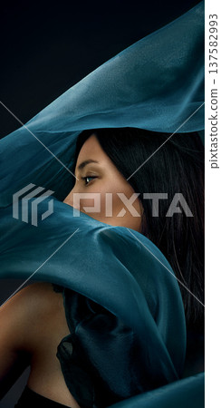 Cinematic portrait of Asian woman partially hidden by flowing teal silk fabric 137582993