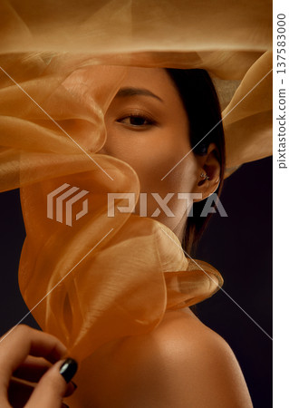 Beauty portrait of Asian woman framed by translucent golden silk fabric with flowing shapes 137583000