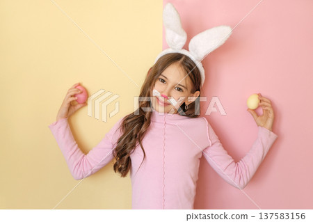 A girl with a painted rabbit face and fluffy ears holds Easter eggs in her hands. Happy Easter Day A girl with a painted rabbit face and fluffy ears holds Easter eggs in her hands. Happy Easter Day 137583156