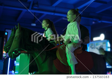 Kids and dad ride an interactive horse in an amusement park Kids and dad ride an interactive horse in an amusement park 137583163