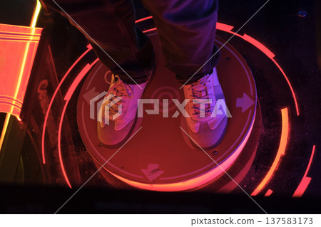 A glowing neon button for an outdoor dance game with arrows in an amusement park. Guy on Dance Pad, Retro Gaming Icon A glowing neon button for an outdoor dance game with arrows in an amusement park. Guy on Dance Pad, Retro Gaming Icon 137583173