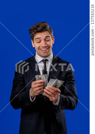 Happy excited businessman counts cash money - USD currency dollars banknotes on blue. Symbol of jackpot, gain, victory, winning the lottery 137583216