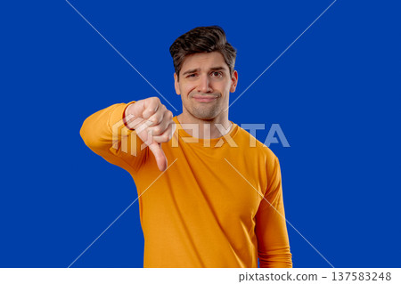 Handsome man In Yellow Wear Giving Thumbs Down Dislike With Disapproving Look Handsome man In Yellow Wear Giving Thumbs Down Dislike With Disapproving Look 137583248