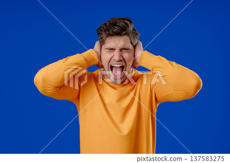 Mature man Covering Ears, Showing Irritation In Blue Studio. Stress, Overload Mature man Covering Ears, Showing Irritation In Blue Studio. Stress, Overload 137583275