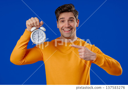 Happy man with alarm clock on blue. Early morning, correct day routine, living in moment, appreciate every minute of life, youth Happy man with alarm clock on blue. Early morning, correct day routine, living in moment, appreciate every minute of life, youth 137583276