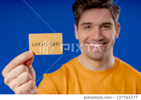 Successful Man In Yellow Outfit Showing Unlimited Gold Credit Card On Blue 137583277