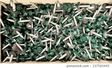 Green roofing screws with rubber washers in box, top view, construction fasteners background. 137583445