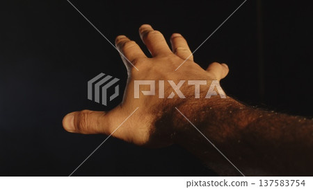 A male hand, fingers spread, stretches into the distance against a black background. A male hand, fingers spread, stretches into the distance against a black background. 137583754