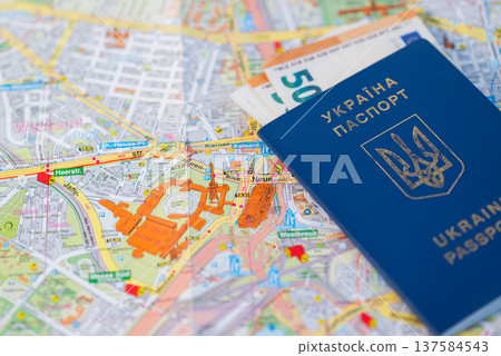 Ukrainian biometric passport with Euro banknotes lying on a travelling map of Berlin, Germany. 137584543