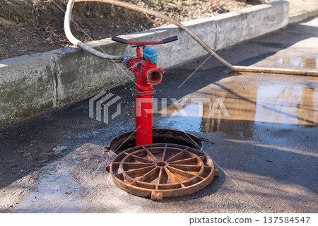 Sewer cleaning process with hydrant and hose in open manhole on city street, municipal drainage maintenance 137584547
