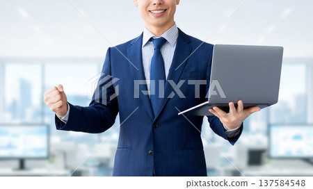 一名手持電腦的男性商人揮拳慶祝。 137584548