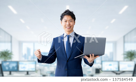 一名手持電腦的男性商人揮拳慶祝。 137584549